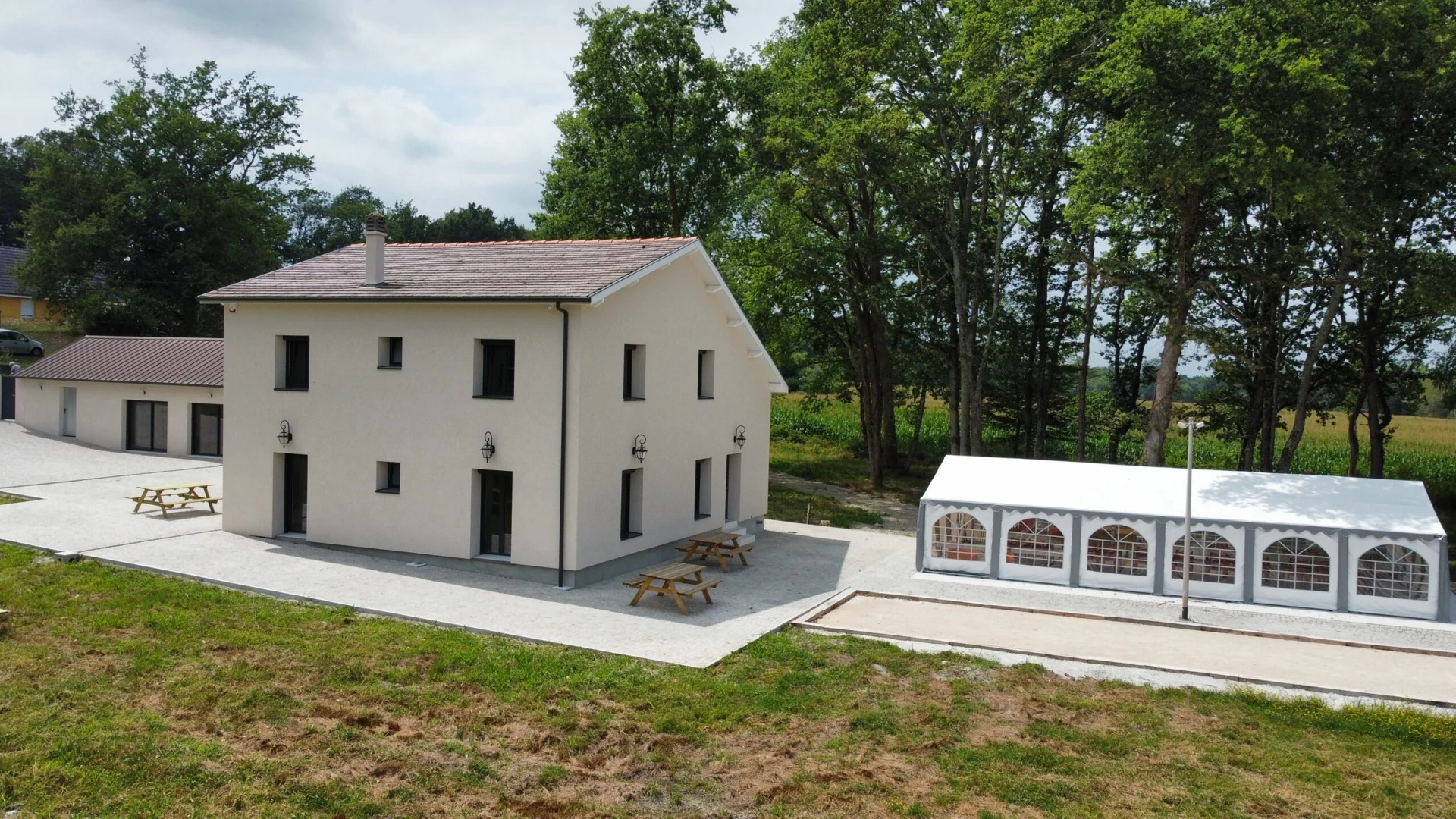 La façade claire de la maison, la terrasse et la tente devant les arbres