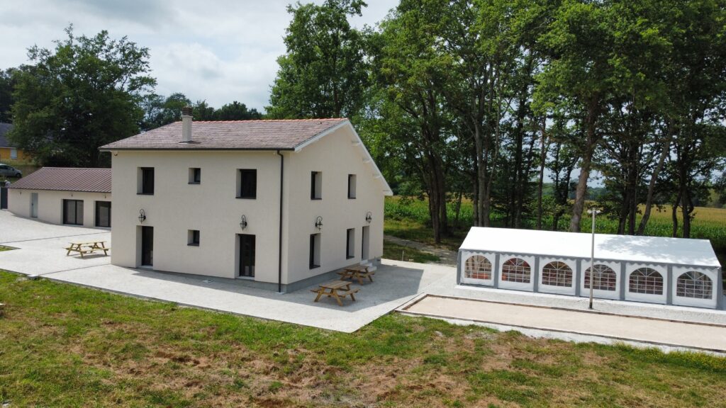 La façade claire de la maison, la terrasse et la tente devant les arbres